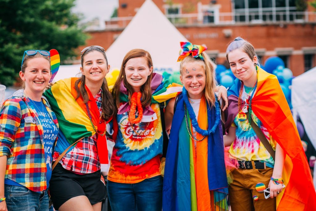 group of friends wearing rainbow clothes smiling at camera
